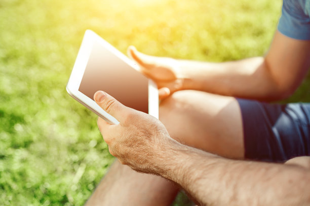 一个穿着休闲的年轻人坐在公园里使用现代数字平板电脑的特写，阳光图片下载