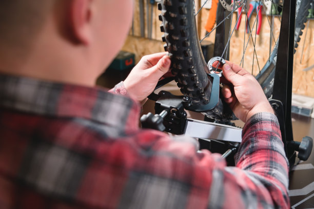 年轻的男性自行车修理工在车间的支架上用一个专门的扳手拧紧车轮的辐条，消除轮辋的跳动图片下载