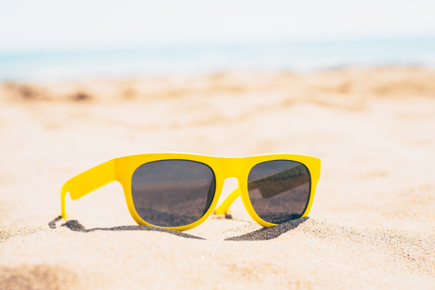 美丽时尚的太阳镜在海滩上对着蔚蓝的水的背景图片下载