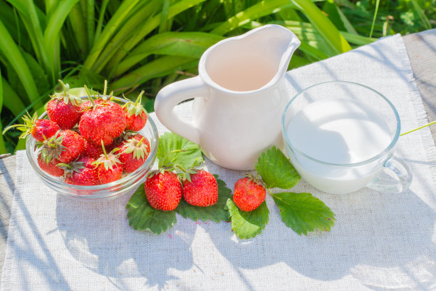 木桌上放着一张餐巾纸，上面放着草莓和树叶，一个罐子和一个盛着牛奶的杯子图片下载