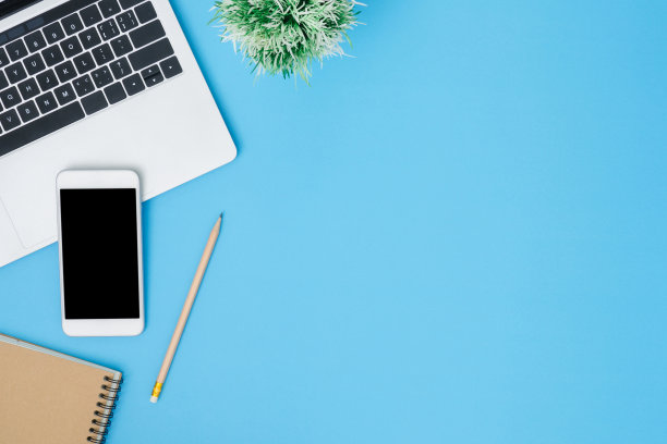 办公室办公桌工作空间-平铺俯视图模型照片的工作空间与笔记本电脑，智能手机和笔记本电脑放置在蓝色蜡笔背景。粉蓝色复制空间办公桌的概念。图片下载