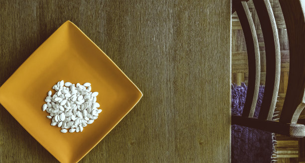 俯视图的南瓜种子在橙色的方形盘子上的天然木桌与椅子-水平直接上方的椅子桌子的南瓜种子图片下载