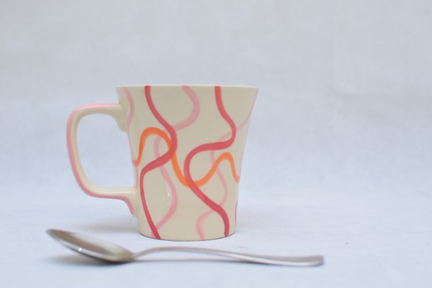 白色背景上用于热饮的彩色陶瓷杯和不锈钢勺图片下载