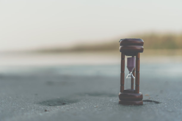 小小的沙漏显示时间在美丽的沙滩上流淌。图片下载