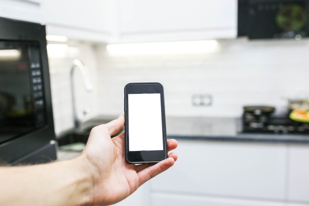 智能家居系统。厨房背景上有白色屏幕的智能手机。图片下载
