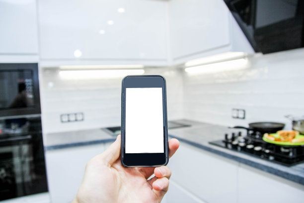 智能家居系统。厨房背景上有白色屏幕的智能手机。图片下载