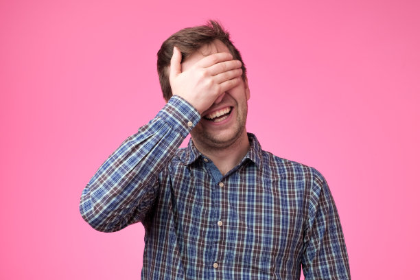 年轻英俊的男子笑着，手捂着脸捂着眼睛，惊讶不已图片下载