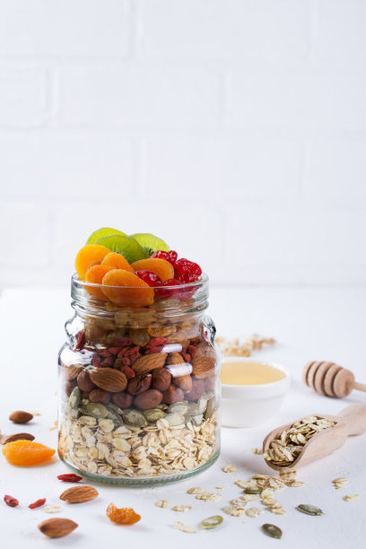 白色背景上的玻璃罐，里面有烹饪格兰诺拉麦片的原料。燕麦片，蜂蜜，坚果，干果和种子。健康snak图片下载