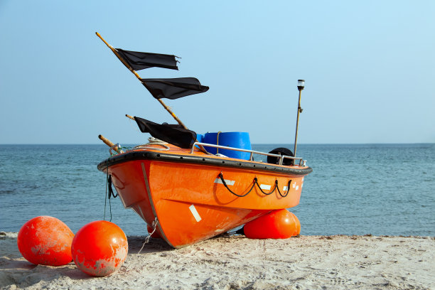 海滩上挂着黑色旗帜的橙色渔船图片下载