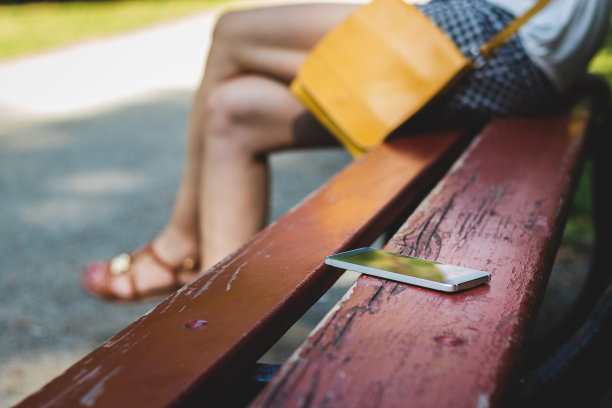 一个女人坐在公园里，把手机忘在长椅上。图片下载