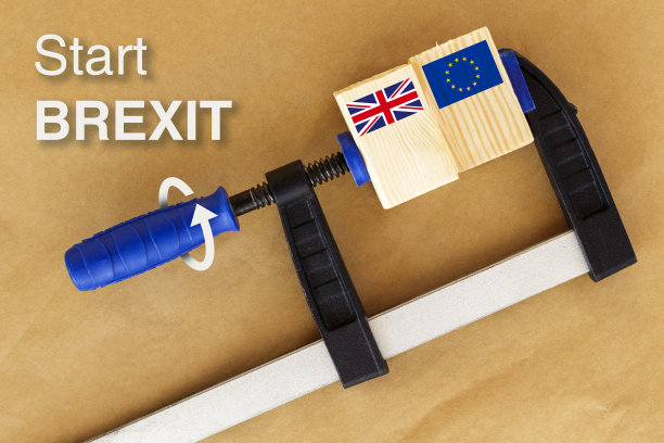 文字“Start BREXIT”，夹紧两块木头，牛皮纸背景上印有欧盟和英国国旗。箭头指示释放木片的方法图片下载