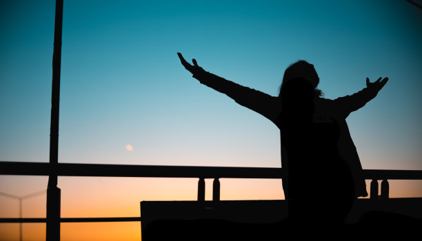 日落时分，一个留着长发的年轻人张开双臂的剪影图片下载
