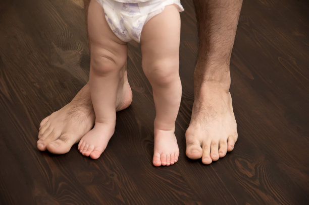 孩子迈出了第一步。雄性的大腿和婴儿的小腿。爸爸帮助孩子迈出第一步。图片下载