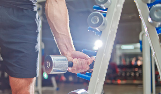 一个年轻人正在从体育馆的架子上取下静脉血手轻金属哑铃图片下载