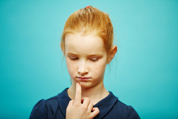 一个小女孩的肖像，生气的脸向下看，若有所思地把她的手指放在下巴，表示关心或悲伤。图片下载