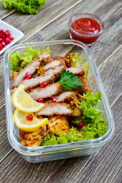 木桌上的玻璃碗里盛着烤土豆、肉、青菜和辣酱的热沙拉。午餐盒。图片下载