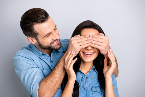 近距离的照片惊人的她她他他他的夫妇女人男人隐藏眼睛猜谁的游戏准备浪漫惊喜的夜晚晚上穿休闲牛仔裤牛仔衬衫套装衣服孤立的灰色背景图片下载