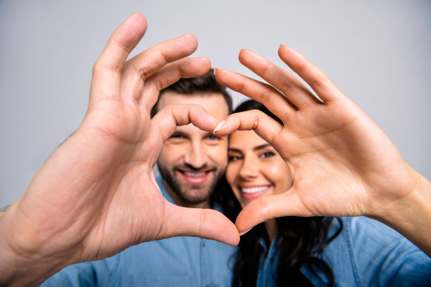 这是一对快乐的学生情侣的特写照片，他们把手指放在心里，在银色的背景下穿着牛仔夹克，感受孤独的幸福图片下载