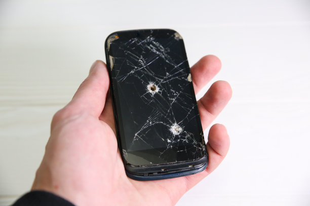 一名男子手持坠毁的黑色智能手机，手里拿着一个弹孔。液晶触摸屏破碎。信息技术的照片。战争的概念。图片下载