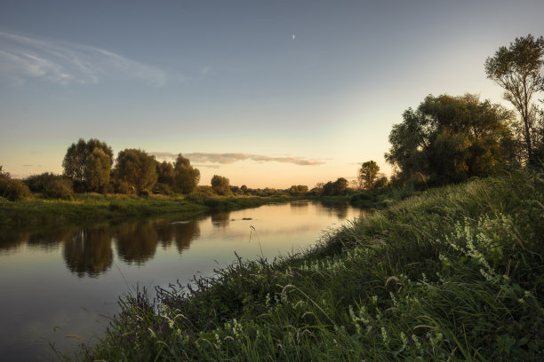狭窄的河流夏季风景景观与宁静的水镜日落与清澈的天空和倒影的河岸图片下载