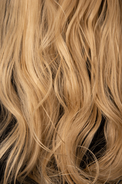 金发红褐色的女士头发。卷毛的，在黑色套头衫的背景下洗得有点湿。有波浪和明亮颜色的长发。图片下载