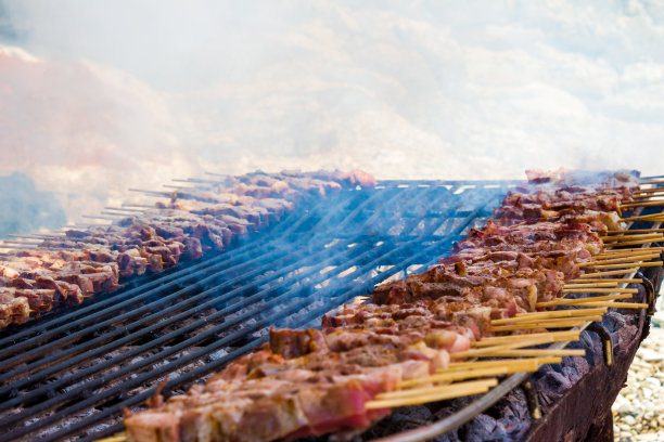 在一个希腊小岛的沙滩上，摆放着一个简单的乡村烤架，上面放着鸡肉和羊肉串。熏制肉类的特写。图片下载