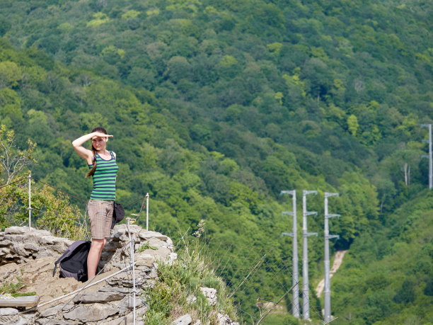 一个女孩站在悬崖上，以绿色的森林为背景图片下载