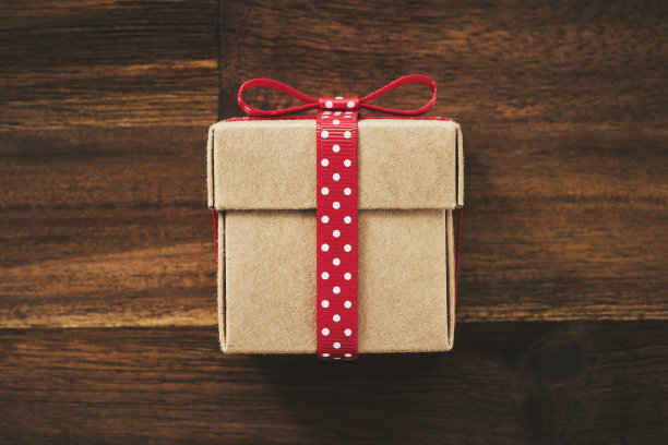 圣诞贺卡与你的文字的地方。礼物在一盒牛皮纸与红色丝带绑在中间的特写背景棕色旧的破旧木板为您的设计。复古的图片图片下载