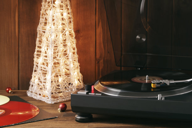 圣诞节的照片。红黑胶唱片在转盘上旋转的瞬间，带有针的唱针落在黑胶唱片上，背景音乐是一棵发光的圣诞树，上面有红色的玻璃球图片下载