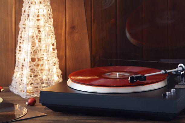 圣诞节的照片。红黑胶唱片在转盘上旋转的瞬间，带有针的唱针落在黑胶唱片上，背景音乐是一棵发光的圣诞树，上面有红色的玻璃球图片下载