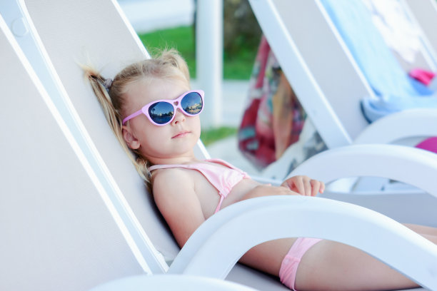 一个戴着墨镜的小女孩在甲板上的椅子上晒日光浴。一个漂亮的婴儿正在休息。明亮的夏天的照片。图片下载