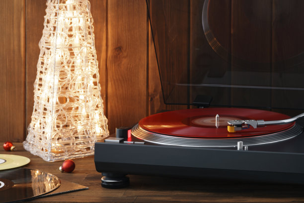圣诞节的照片。红黑胶唱片在转盘上旋转的瞬间，带有针的唱针落在黑胶唱片上，背景音乐是一棵发光的圣诞树，上面有红色的玻璃球图片下载