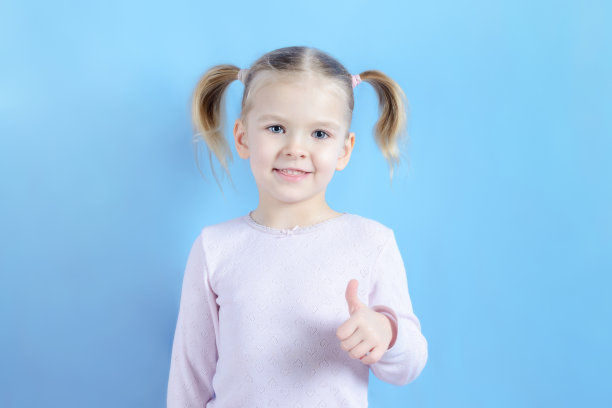 金发小女孩做了个超级手势。蓝色背景下一个快乐的孩子的照片。光照片。图片下载