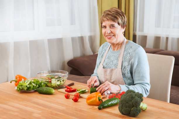 年长的妇女在厨房里做沙拉，看着镜头。健康食品的概念。健康的生活方式。图片下载