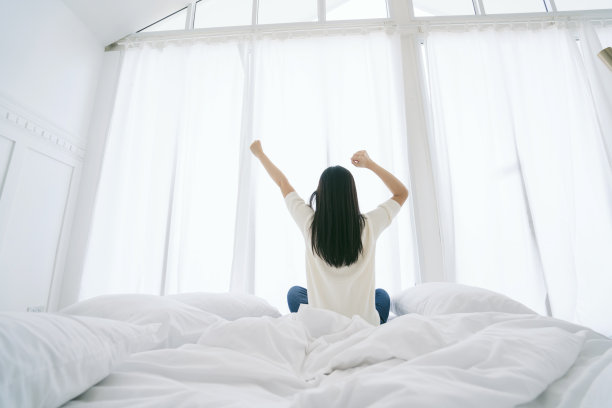 白色连衣裙亚洲美丽的女人伸展早晨醒来卧室与白色窗帘的背景生活方式家的概念图片下载