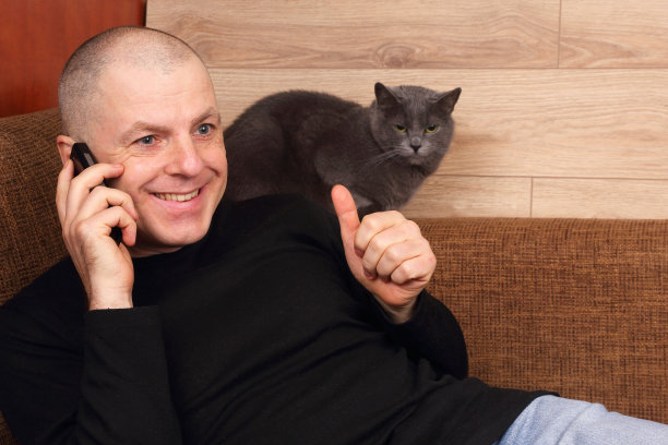 男人情绪化地讲电话，和猫休息在沙发上图片下载