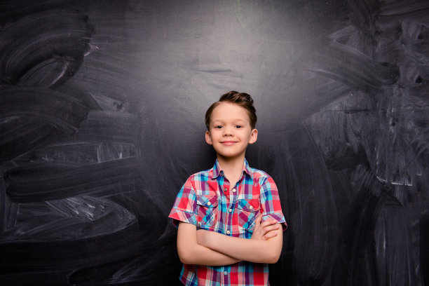 小男孩双手交叉放在黑板的背景上图片下载