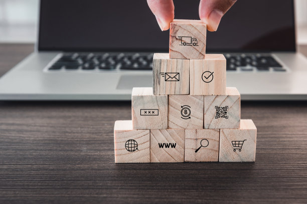 商业电子商务和购物媒体图标的概念，特写手指男人是从电脑笔记本电脑前的堆栈上捡起的木制立方体。图片下载