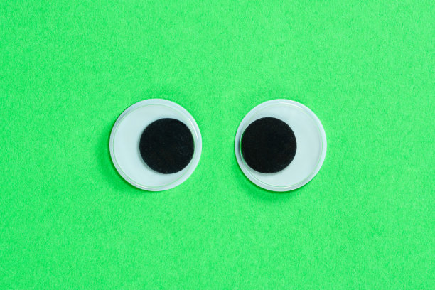 在霓虹绿色背景上的斗鸡眼。疯狂有趣的玩具眼睛合上。图片下载