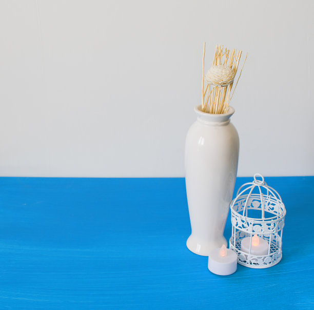 房子的室内装饰，白色和蓝色背景上的鲜花、蜡烛、花瓶、鸟笼。静物自然图片下载