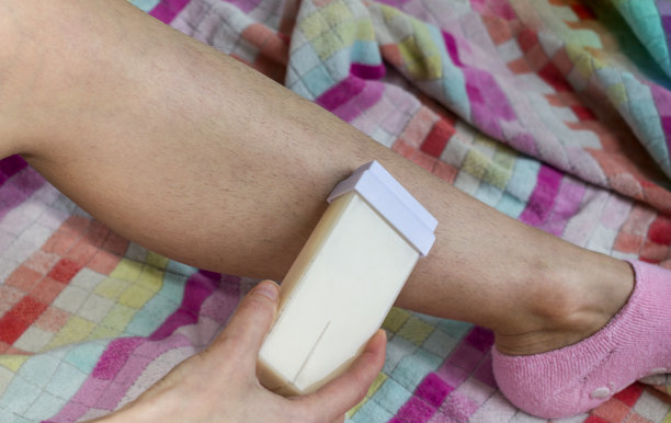 女人和她毛茸茸的腿在一条多色毛巾上。女孩用蜡进行脱毛。图片下载