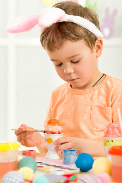 带着复活节兔子耳朵的小男孩在画复活节彩蛋图片下载