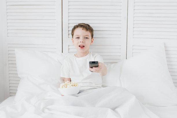 男孩坐在床上看电视，吃着爆米花图片下载