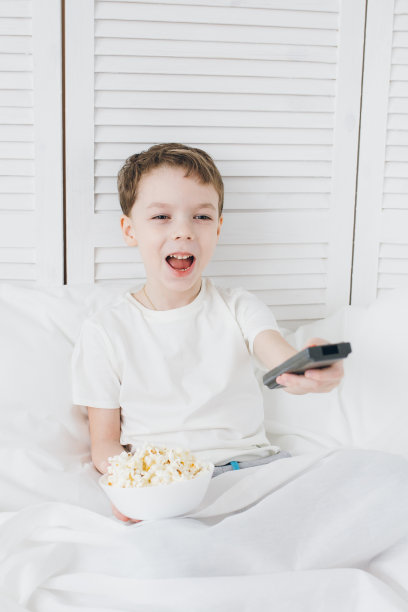男孩坐在床上看电视，吃着爆米花图片下载