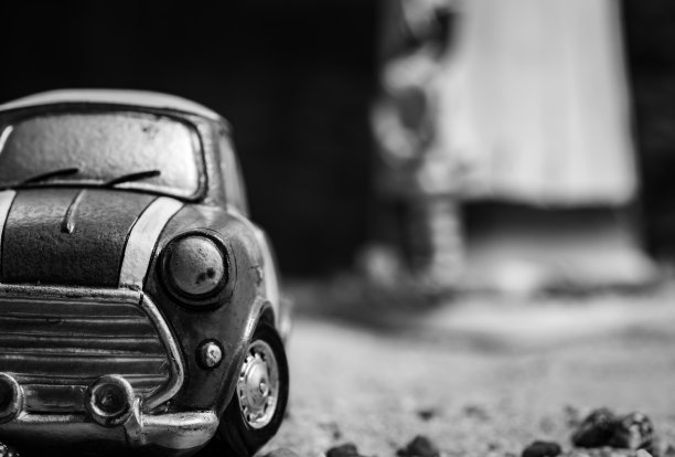 沙路上小汽车玩具模型的正面视图。黑白迷你汽车玩具上模糊的背景。卡通微型汽车。想象的世界。第一辆车的概念。汽车租赁及保险。图片下载