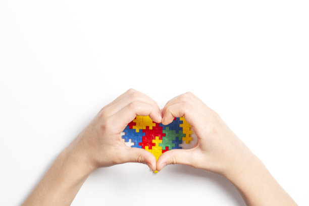 孩子的手在形状的心和彩色的心塑料建设拼图块在白色的背景。世界自闭症宣传日的概念图片下载