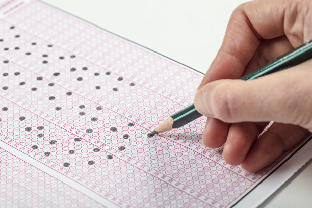 高中生或大学生手拿试卷，在答题纸上写试卷，标准化考试光学形式放在桌上，在教室里做期末考试。教育素养的概念。图片下载