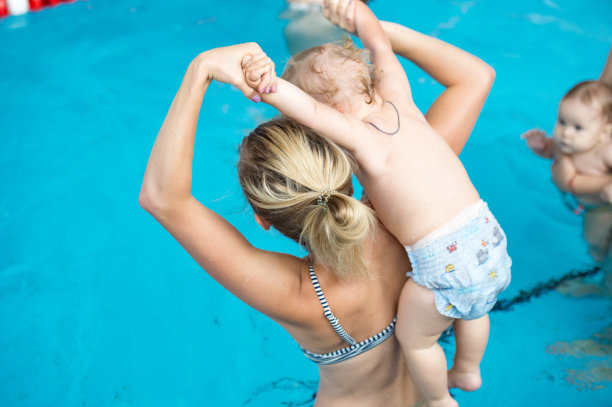 在炎热的夏天，快乐的年轻妈妈和她的孩子在游泳池里玩。孩子们在家庭度假时学习游泳。妈妈和孩子在水里玩。图片下载