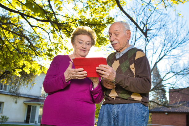 退休社区的概念。快乐的退休老人夫妇微笑着看着平板电脑上孙辈的照片图片下载
