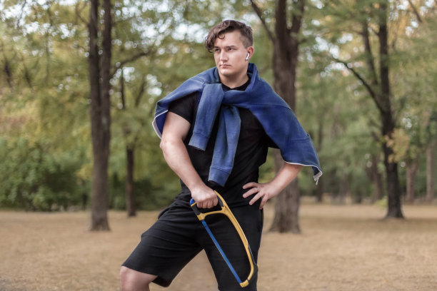 年轻有吸引力的性感男子与深色卷发站在森林手锯。休闲装，白色耳机，耳环。户外，美丽的秋日背景，金色的树叶。幽默,有趣的图片图片下载